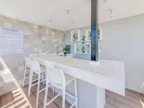 A modern kitchen with a marble countertop, white chairs, and a backsplash with patterned tiles. - Penthouse Hermosa Con Terraza en Zona Dorada (Mazatlán)