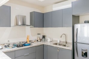 A modern kitchen with grey cabinets, a stainless steel range hood, a built-in sink, and a refrigerator. - Penthouse Hermosa Con Terraza en Zona Dorada (Mazatlán)