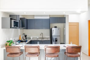A modern kitchen with grey cabinets, a stainless steel refrigerator, and a built-in microwave. There are four brown chairs around a table. - Penthouse Hermosa Con Terraza en Zona Dorada (Mazatlán)