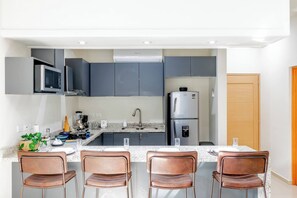 Une cuisine moderne avec des meubles gris, un réfrigérateur en acier inoxydable et un coin repas équipé de quatre chaises.