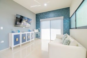A modern living room with a flat-screen TV, a white sofa, a blue patterned wall, and a sliding glass door.