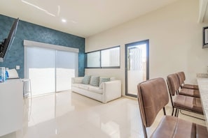 Un salon moderne avec un canapé blanc, un coin repas avec des chaises marron et un escalier.