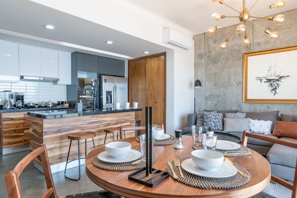 Una cocina moderna con una isla central, comedor con una mesa redonda y una sala de estar con un sofá y un cuadro en la pared.