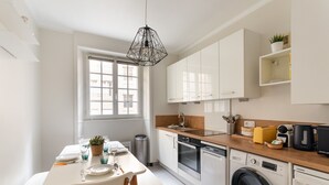 A modern kitchen with white cabinets, a wooden countertop, a washing machine, and a dining area with a table and chairs. - Chez Léon - Appt à 500m des plages (Saint-Malo)