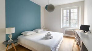 A modern bedroom with a bed, bedside table, lamp, and a desk with a computer. - Chez Léon - Appt à 500m des plages (Saint-Malo)
