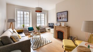 A spacious living room with a sofa, armchairs, a fireplace, and large windows. - Chez Léon - Appt à 500m des plages (Saint-Malo)