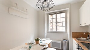 A modern kitchen with white cabinetry, a dining table set for four, and a window providing natural light. - Chez Léon - Appt à 500m des plages (Saint-Malo)
