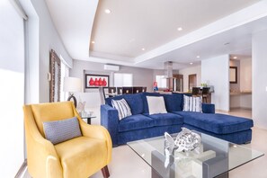 A modern living room with a blue sofa, a yellow armchair, and a glass coffee table.