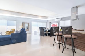 A modern living room with a blue sofa, yellow armchair, and a dining area with bar stools.