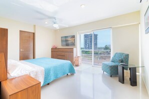 Una camera da letto con un letto, una sedia, un tavolino, una ventola a soffitto, una finestra e un quadro appeso al muro.