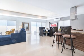 A modern living room with a blue sofa, yellow armchair, and a dining area with bar stools.