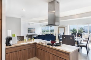 A modern kitchen with a central island, a dining area with a table and chairs, and a living area with a sofa and TV.