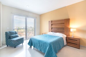 A bedroom with a bed, a nightstand, a chair, and a large window. - Grande Condo 1 Cuadra de Playa En Nuevo Mazatlan (Mazatlán)