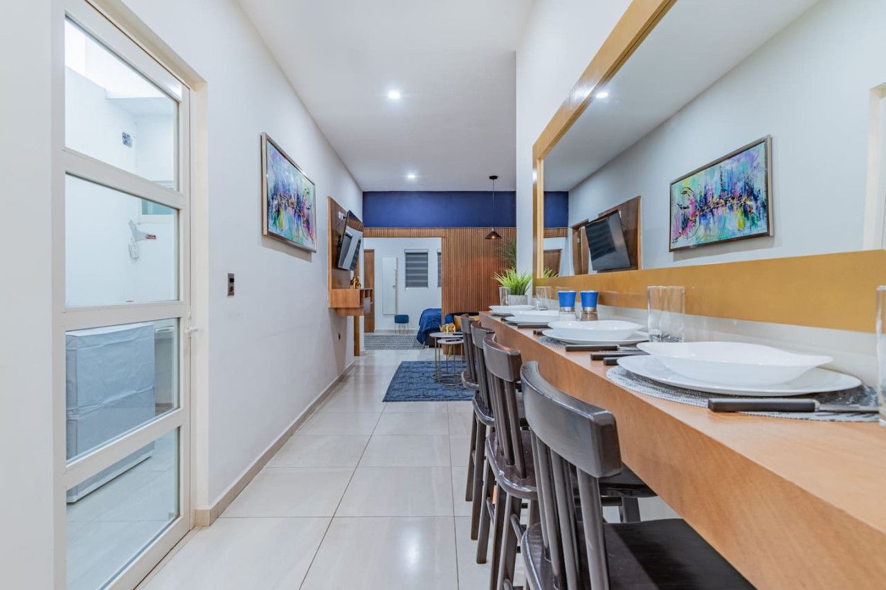 Uma área de jantar moderna com uma mesa comprida, cadeiras e uma TV fixada na parede.