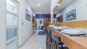 Uma área de jantar moderna com uma mesa comprida, cadeiras e uma TV fixada na parede.