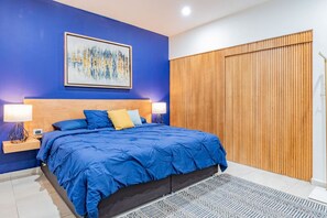 A bedroom with a large bed, a wooden headboard, a blue wall, a wooden partition, and a framed artwork.