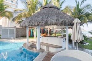 A pool area with a thatched-roof gazebo, palm trees, and a bar. - Lujoso Depa al Pie de la Playa "Camino al Mar" (Mazatlán)
