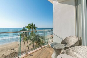 En balkon med udsigt over stranden og havet, møbler i flet og gelænder i glas.