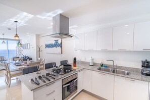 Een moderne keuken met een centraal eiland, roestvrijstalen apparatuur en uitzicht op de woonkamer.