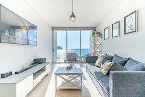 Un salon moderne avec une grande télévision, un canapé, une table basse et une vue sur la mer.