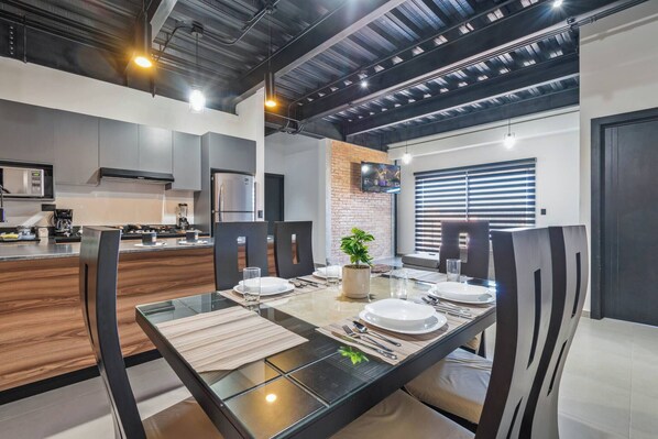 A modern kitchen with a dining area, featuring a glass table, chairs, and a brick accent wall.