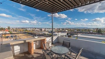 A rooftop terrace with a table and chairs, a barbecue area, and a view of a cityscape.