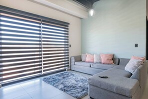 A modern living room with a grey sofa, a fluffy rug, and a large window with blinds.