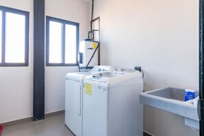 A laundry room with two front-loading washing machines, a water heater, and a utility sink.