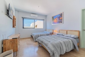 Une chambre avec deux lits, un bureau, une fenêtre, un climatiseur et un tableau.