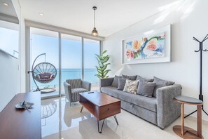 A modern living room with a sofa, a coffee table, a hanging chair, and a large window with a view of the sea.