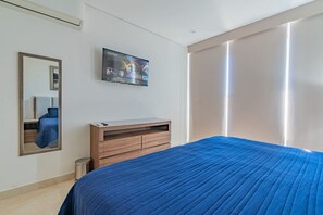 A bedroom with a bed, a TV mounted on the wall, a wooden dresser, and a mirror.