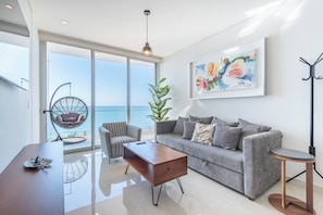 Uma sala de estar moderna com sofá, mesa de centro de madeira, cadeira suspensa e uma janela grande com vista para o mar.