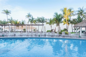 Uma área de piscina com espreguiçadeiras, palmeiras e vista para o mar.
