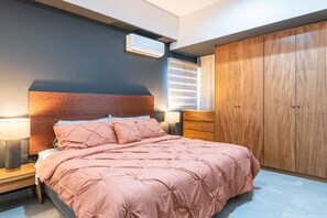 Un dormitorio con cama, lámparas de noche, armario y equipo de aire acondicionado.