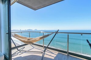 A balcony with a hammock, a view of the ocean, and a clear sky.