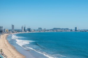 Un paisaje urbano costero con playa, rascacielos y grúas de construcción.