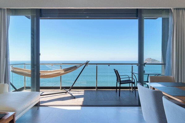 A balcony with a hammock, a sofa, a table, and chairs, overlooking the sea.