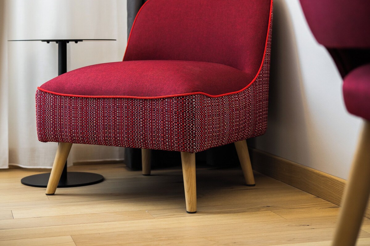 A red chair with a woven seat and wooden legs in a room with a wooden floor and a black table.