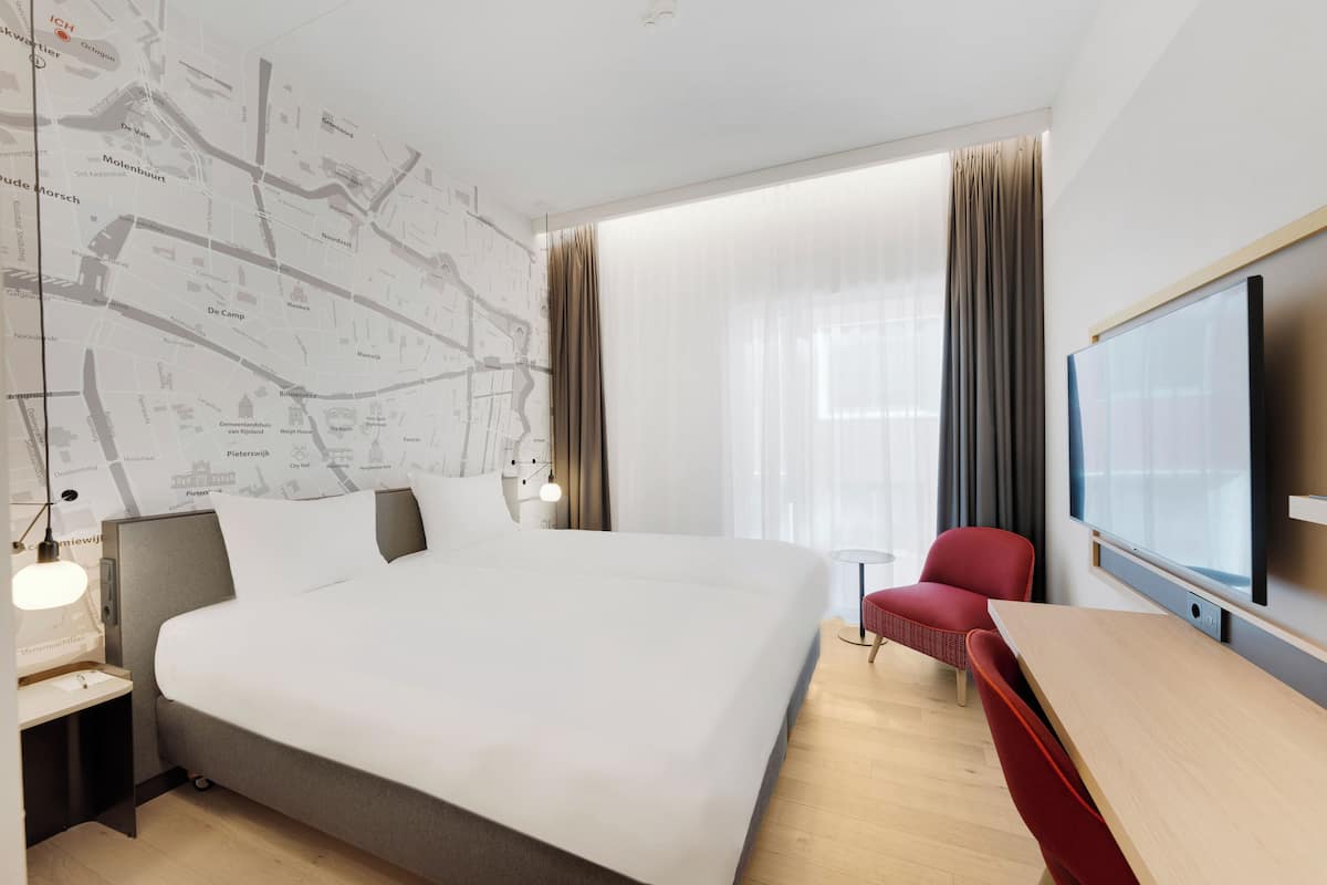 A hotel room with a large bed, a desk, a chair, a TV, and a map on the wall.