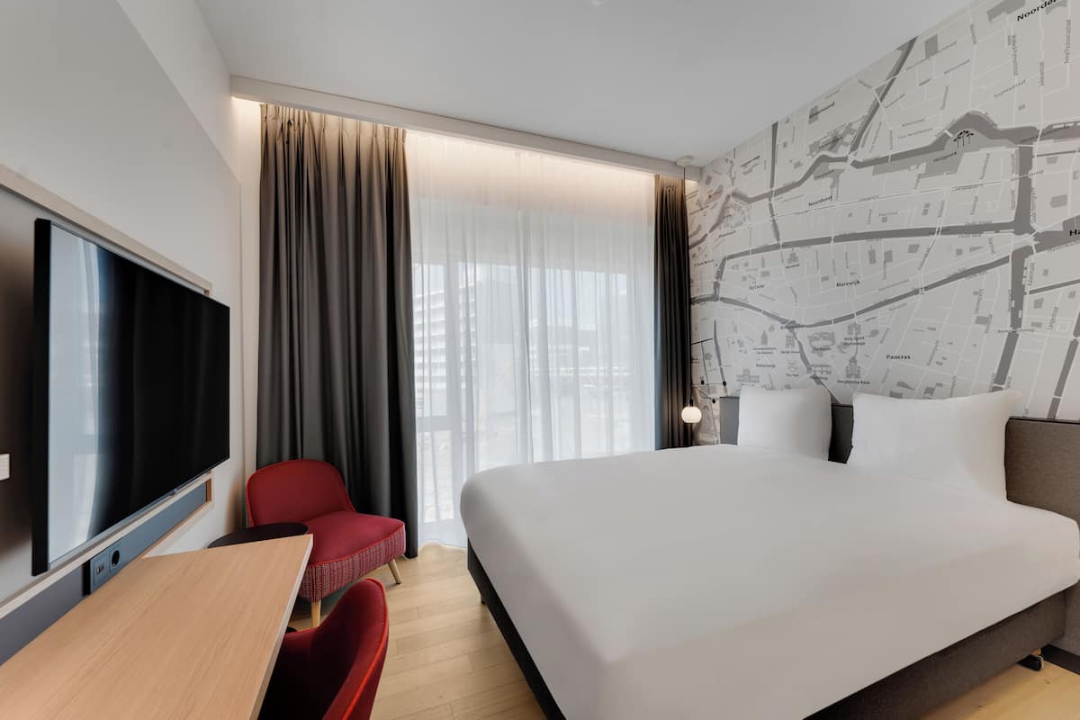 A hotel room with a large bed, a TV, a desk, and a red chair.