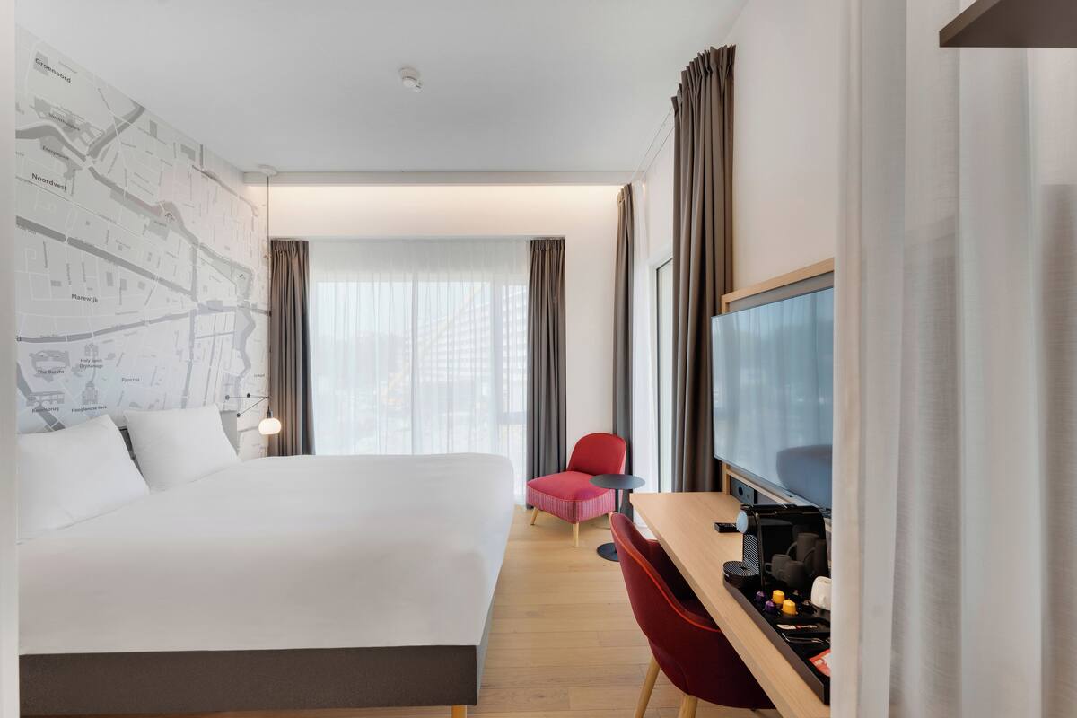 A hotel room with a large bed, a desk with a computer, a chair, and a TV.