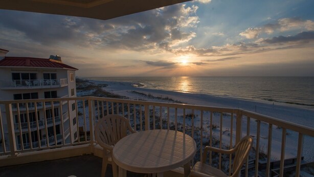 Een balkon met een tafel en stoelen met uitzicht op een strand bij zonsondergang.