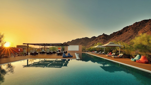 A pool area with lounge chairs and bean bags, a covered seating area, and a view of mountains. - Cloud 7 Residence AlUla (Al-'Ula)