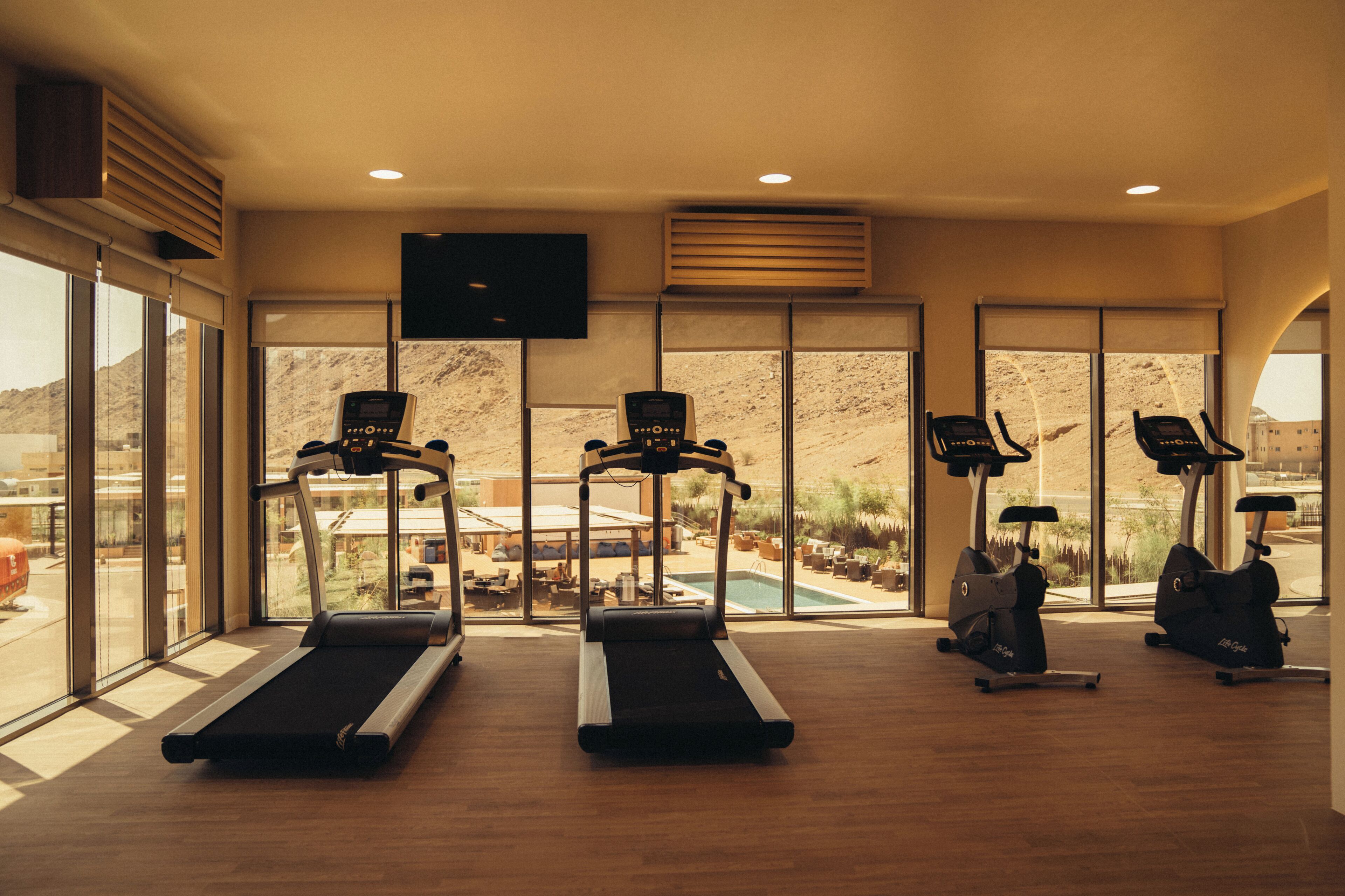 A gym with treadmills, stationary bikes, and a TV screen.