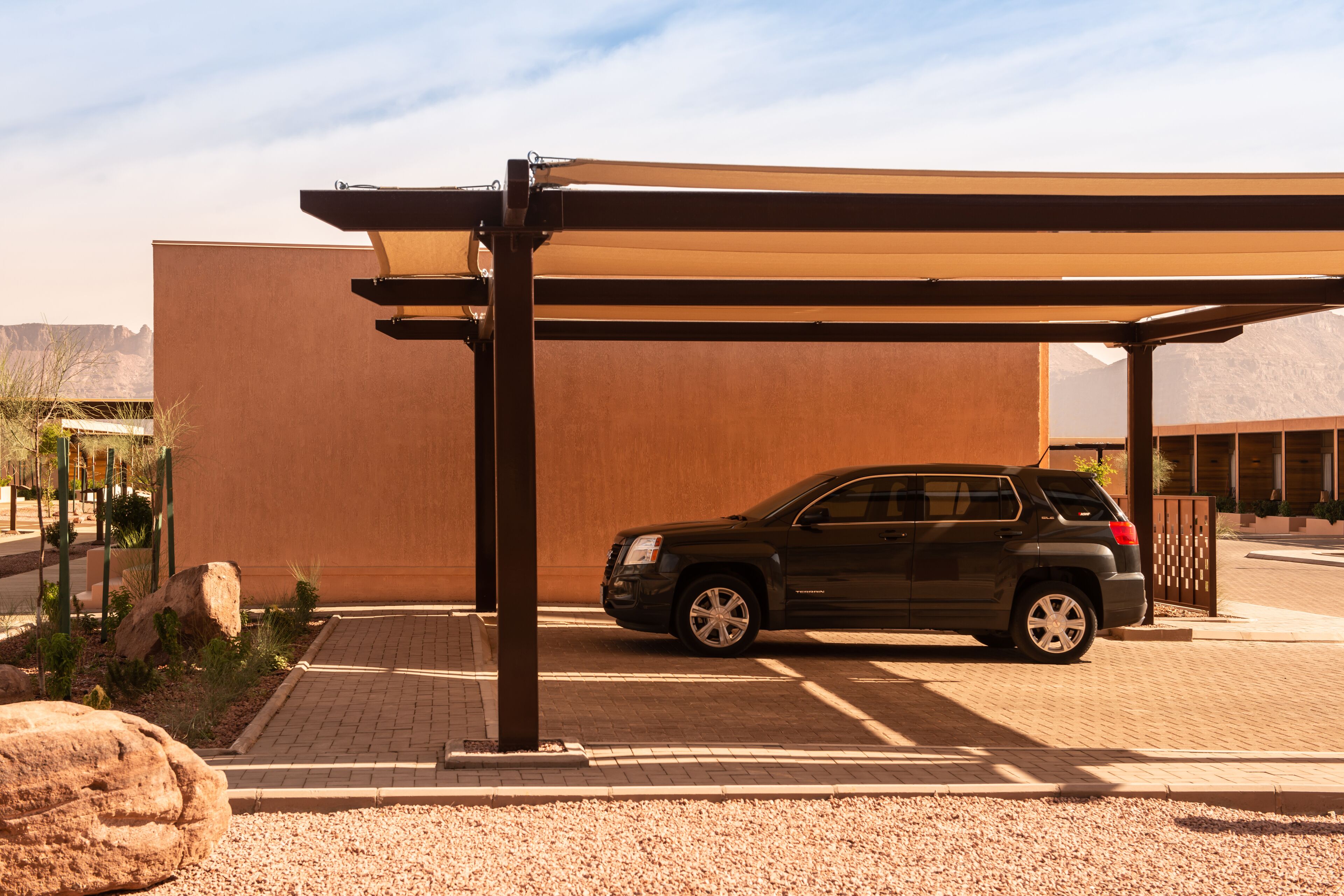 A black SUV parked under a covered area with a large rock and a building in the background.