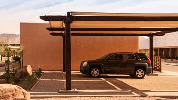 A black SUV parked under a covered area with a large rock and a building in the background.