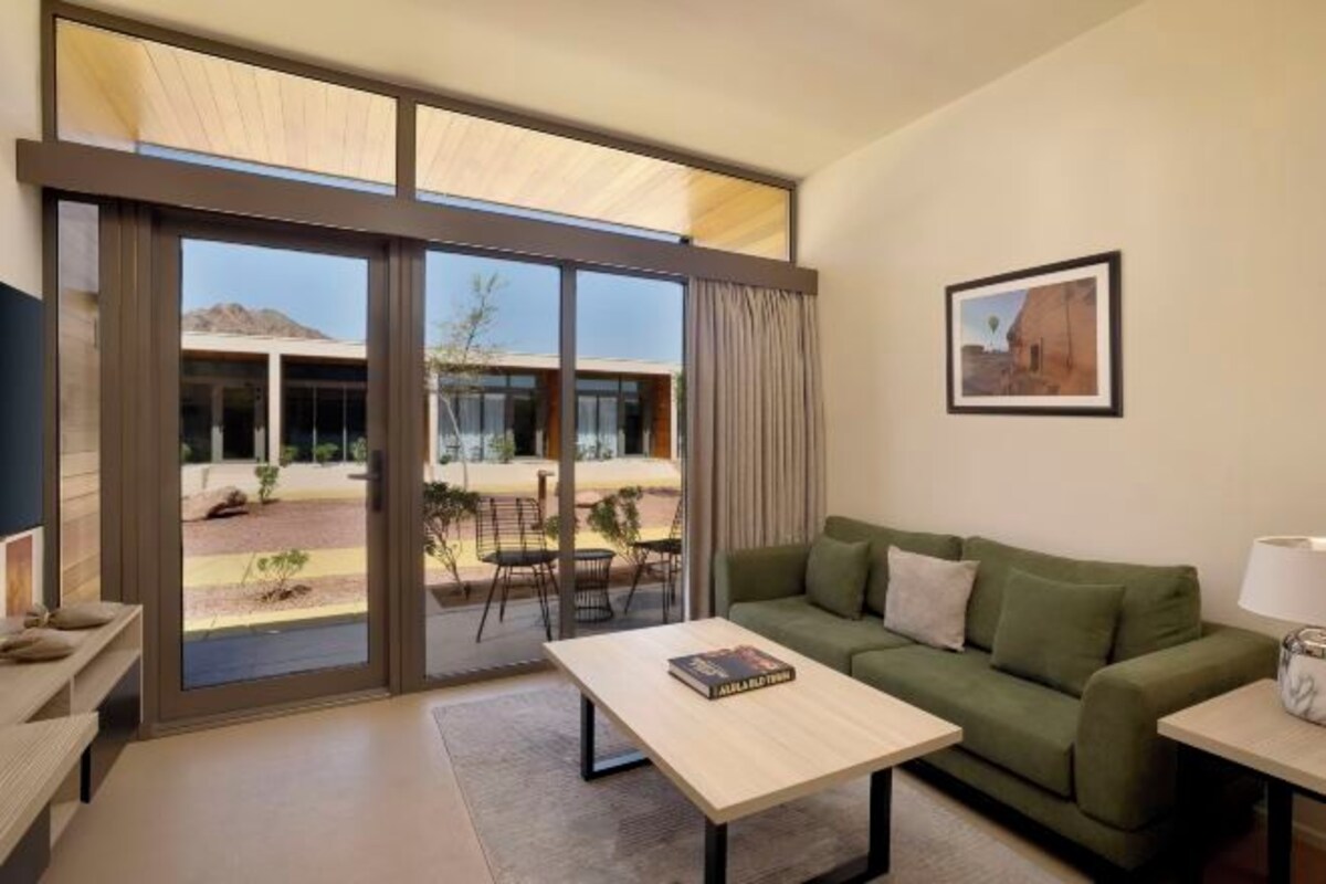 A modern living room with a green sofa, a wooden coffee table, and a large sliding glass door leading to an outdoor area.