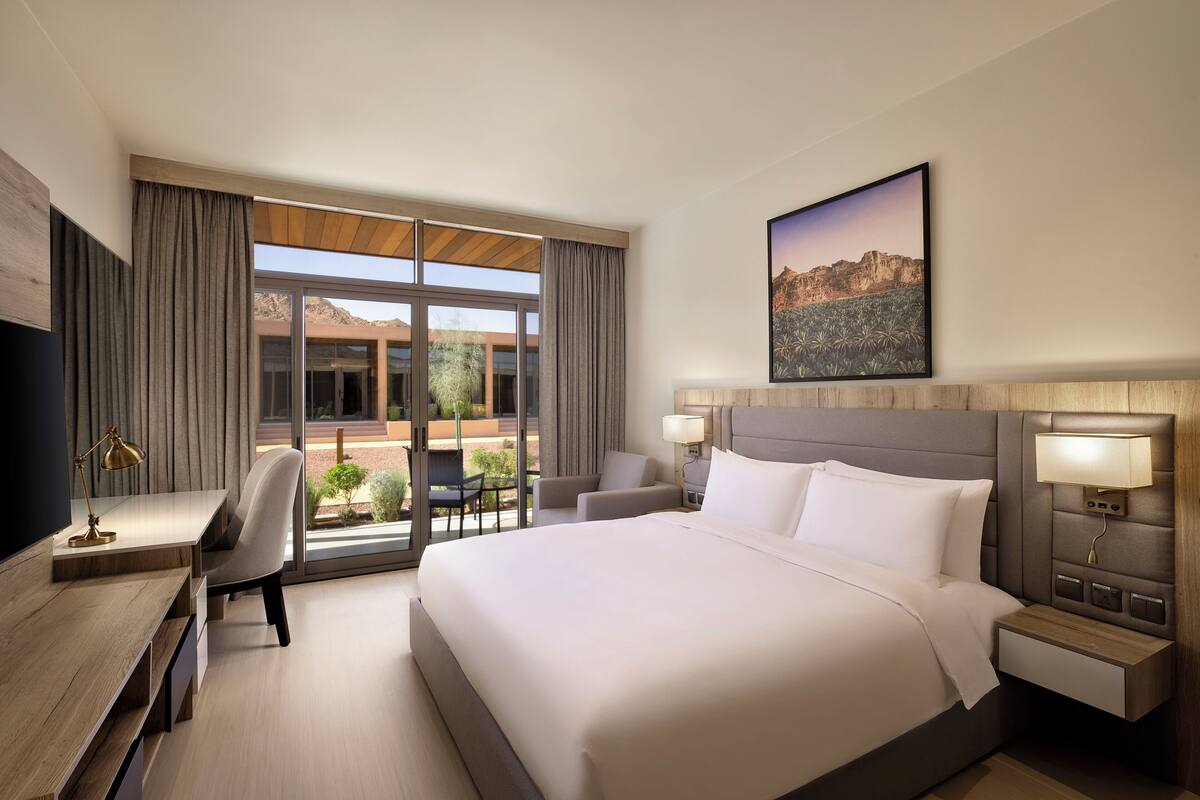 Ein Hotelzimmer mit einem großen Bett, einem Schreibtisch, einem Stuhl und Blick ins Freie.