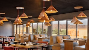A modern restaurant with multiple seating areas, including booths and tables, and large windows offering a view of the landscape. - Cloud 7 Residence AlUla (Al-'Ula)