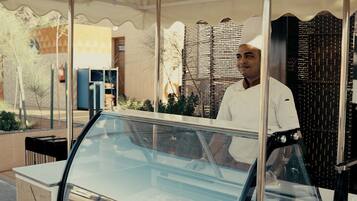 A food truck with a glass enclosure, a man standing behind it, and a sign above that reads "nakhatli".